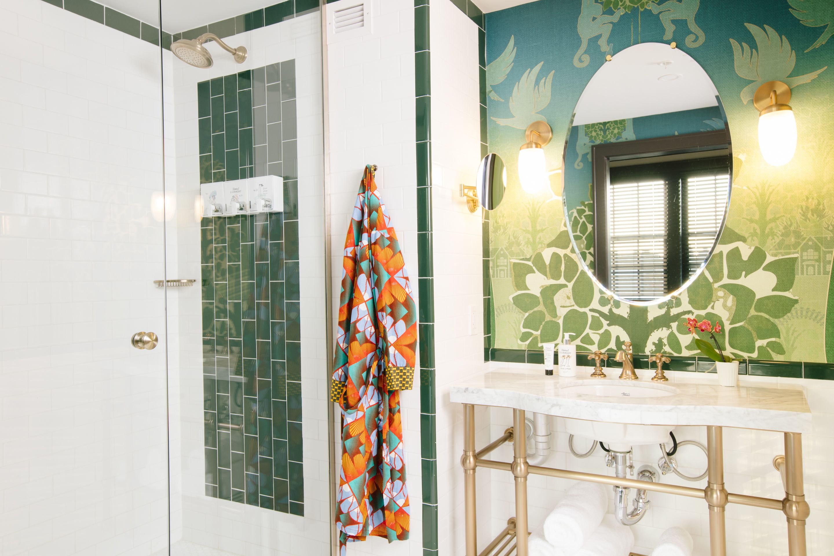 Een badkamer met een douche, een wastafel met spiegel, en een handdoek aan de muur.
