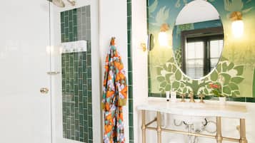Een badkamer met een douche, een wastafel met spiegel, en een handdoek aan de muur.
