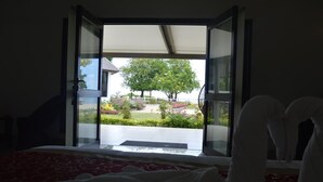 Een hotelkamer met een bed en uitzicht op een tuin door een open deur, evenals een zicht op een gebouw aan de overkant van de straat.