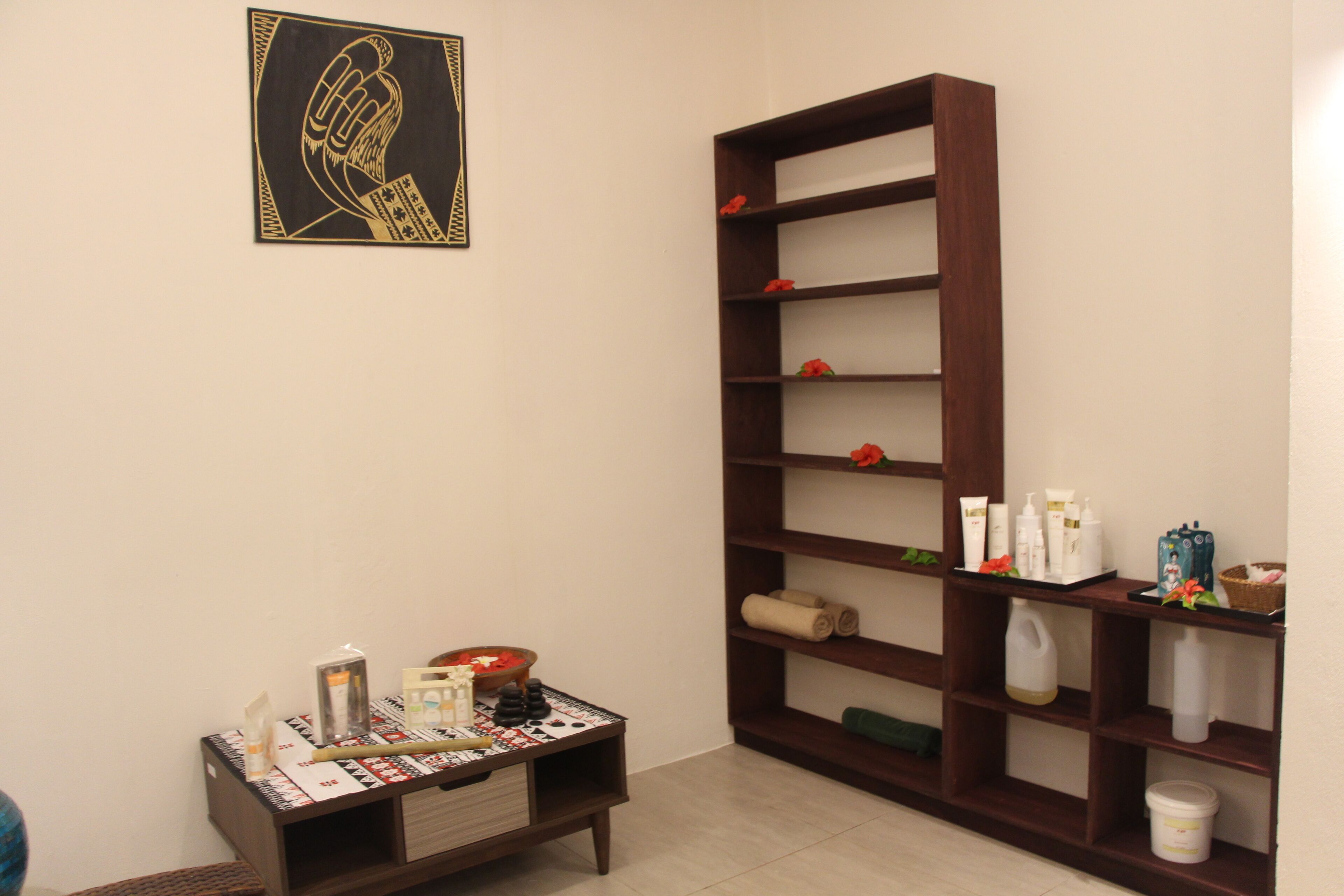 A room with a wooden shelf unit, a small table with toiletries, and a framed artwork on the wall.