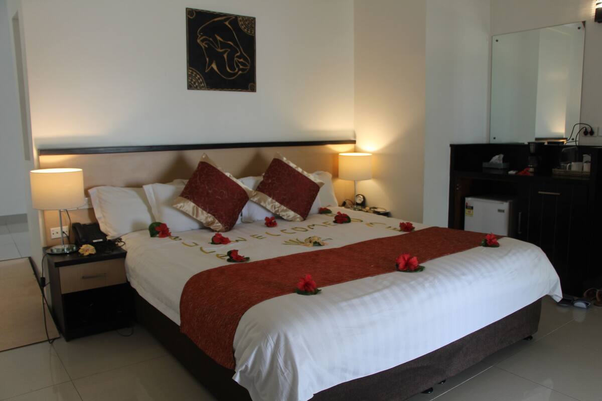 A neatly made bed with a red and white bedspread, two bedside lamps, a nightstand with a phone, and a wall-mounted artwork.