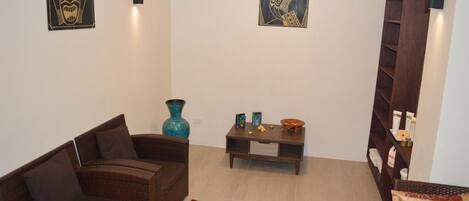 A living room with a brown wicker sofa, a blue vase, and a small wooden table with decorative items.