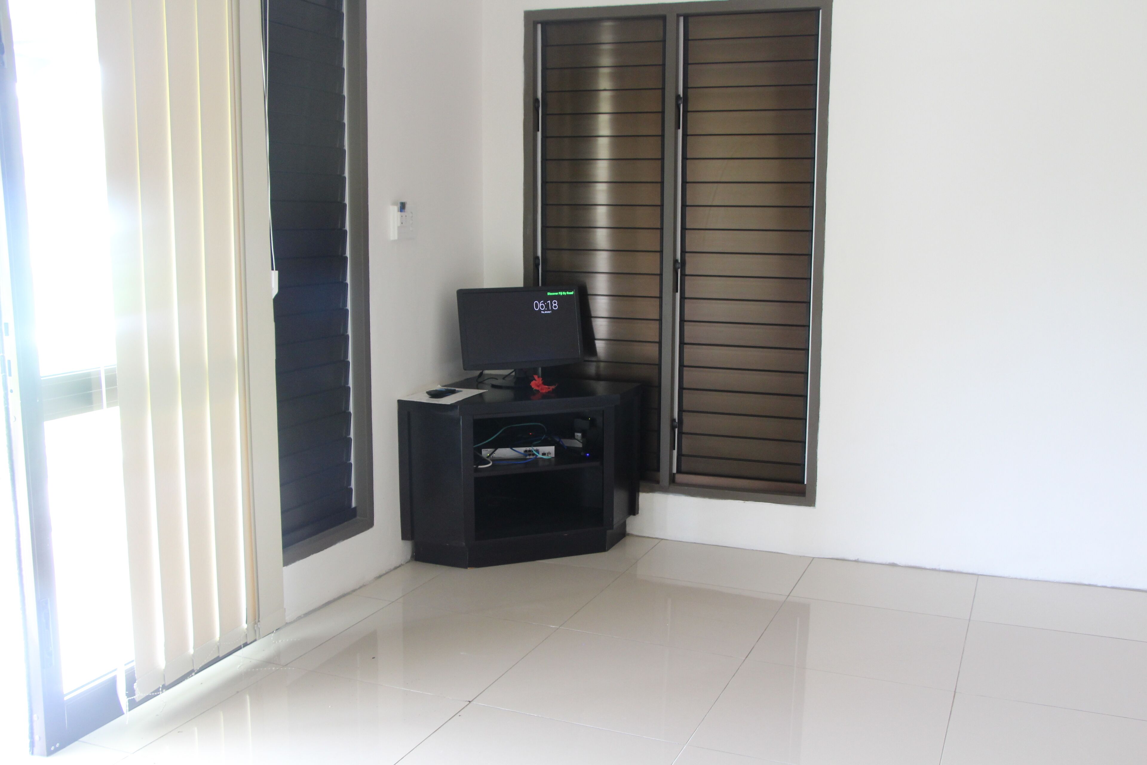 A corner room with a black entertainment unit, a window with blinds, and a door.