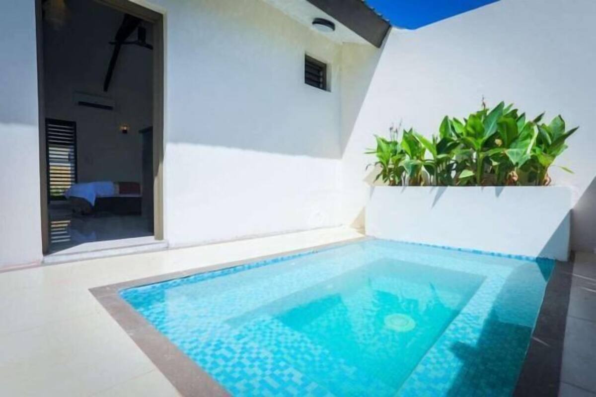 A swimming pool with a tiled edge, a white wall, and a window with blinds.