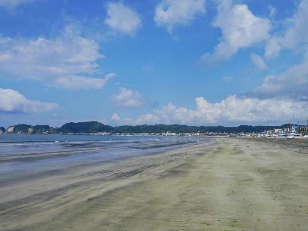 Een breed zandstrand met een heldere lucht en heuvels in de verte.