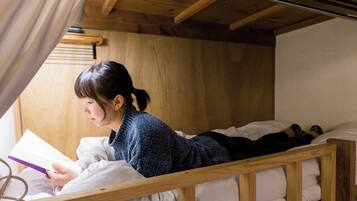 A bunk bed with a person reading a book, wooden walls, and a curtain.