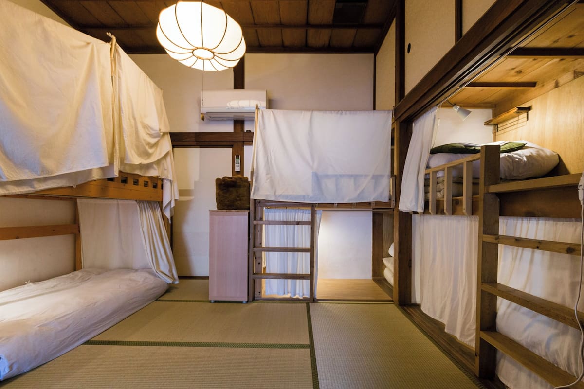 A traditional Japanese-style room with tatami flooring, a wooden bunk bed, a small cabinet, and a ceiling fan.