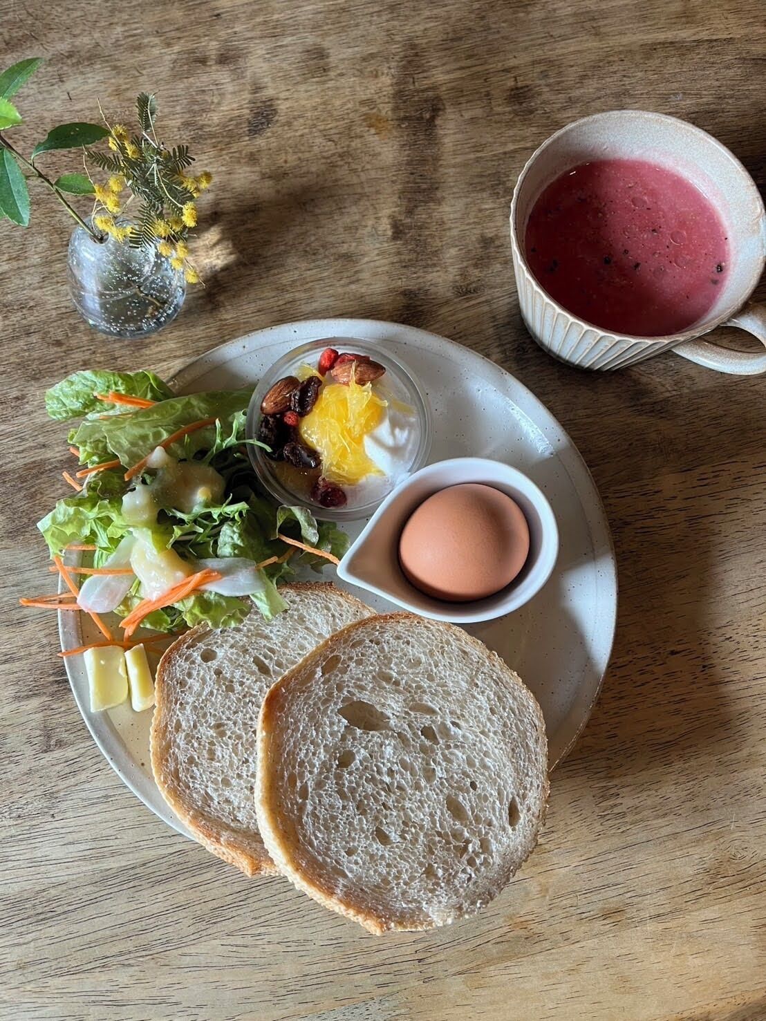 A plate with a salad, a cup of smoothie, a boiled egg, and slices of bread on a wooden table.