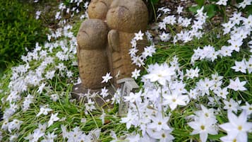 Un jardín con una escultura de piedra que representa a una familia, rodeado de flores blancas.