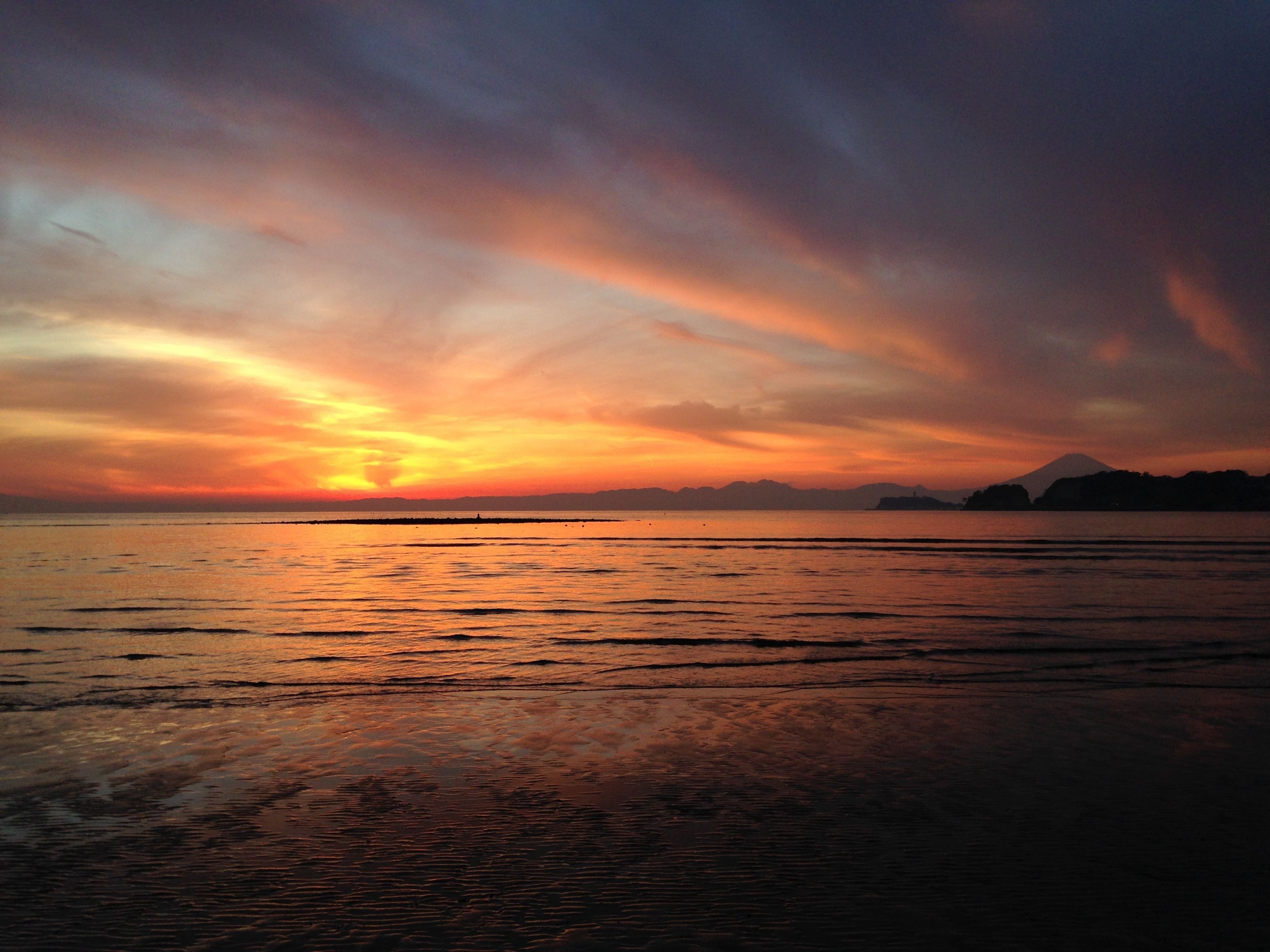 Un atardecer sobre un mar tranquilo, con formas de tierra a lo lejos.