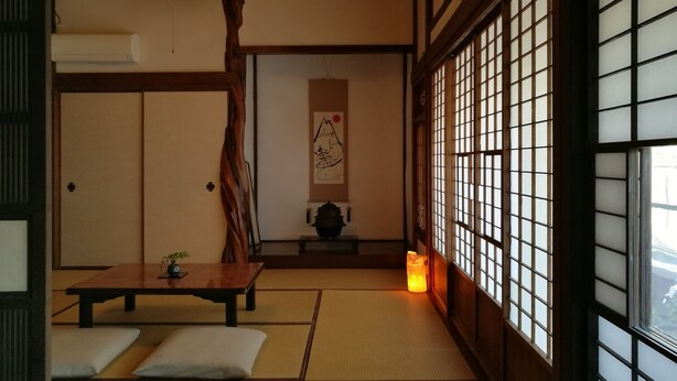 Una habitación japonesa tradicional con suelo de tatami, una mesa baja, cojines, un farol colgante y paneles shoji.