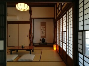 Una habitación japonesa tradicional con suelo de tatami, una mesa baja, cojines, un farol colgante y paneles shoji.