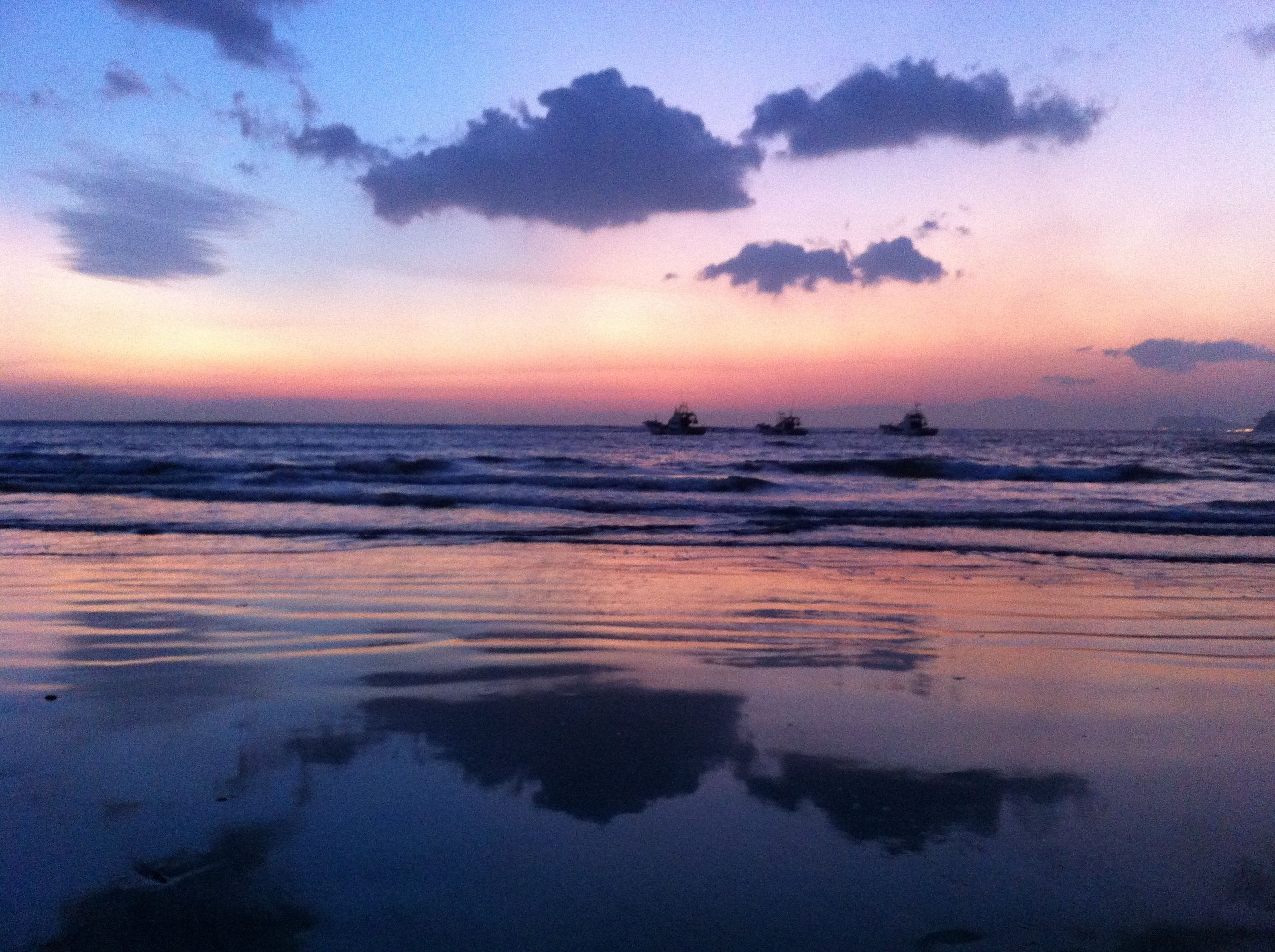 A beach with calm waters and boats in the distance.