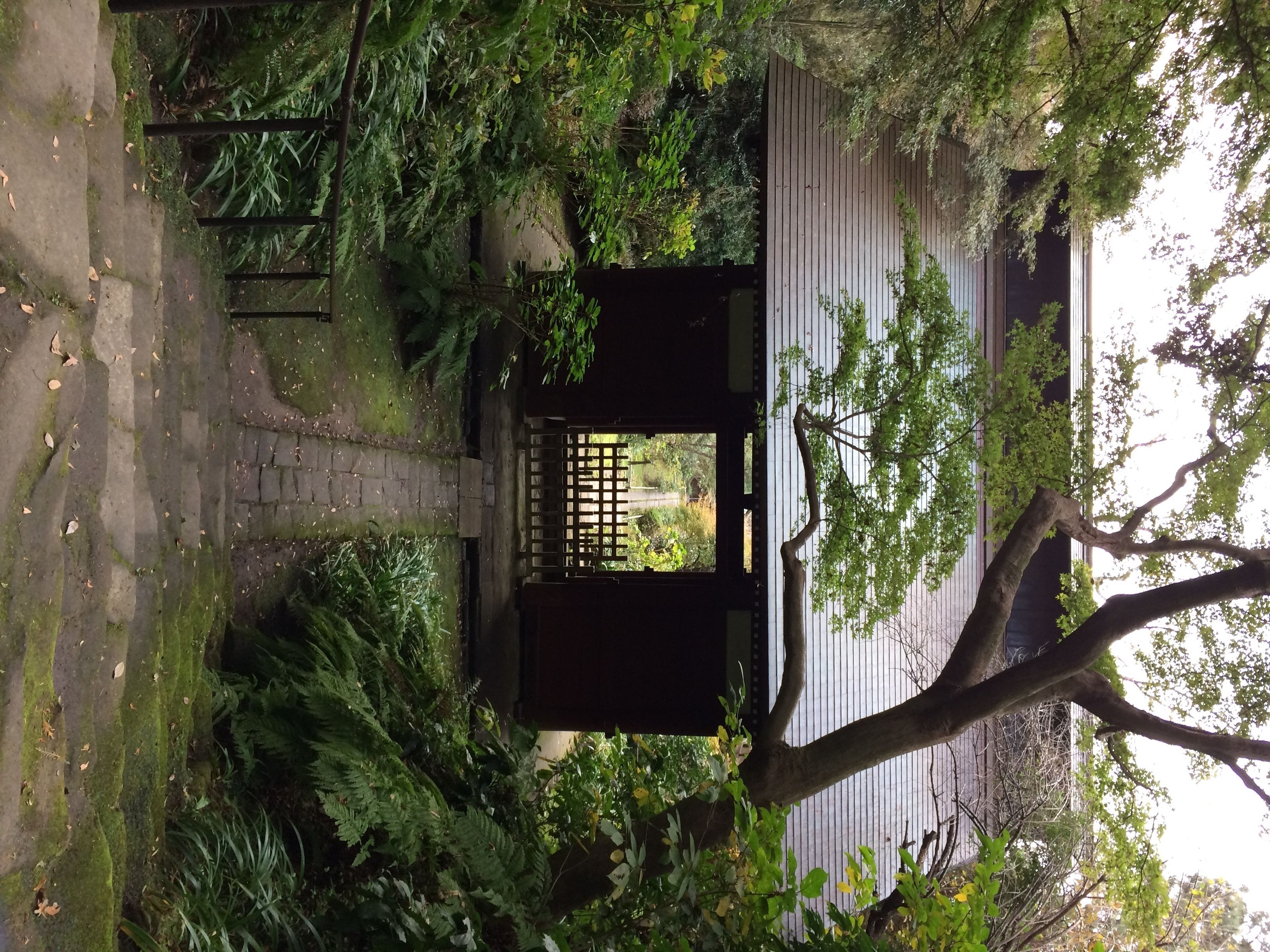 A traditional Japanese gate with a wooden structure and a lattice design, surrounded by lush greenery and a stone pathway.