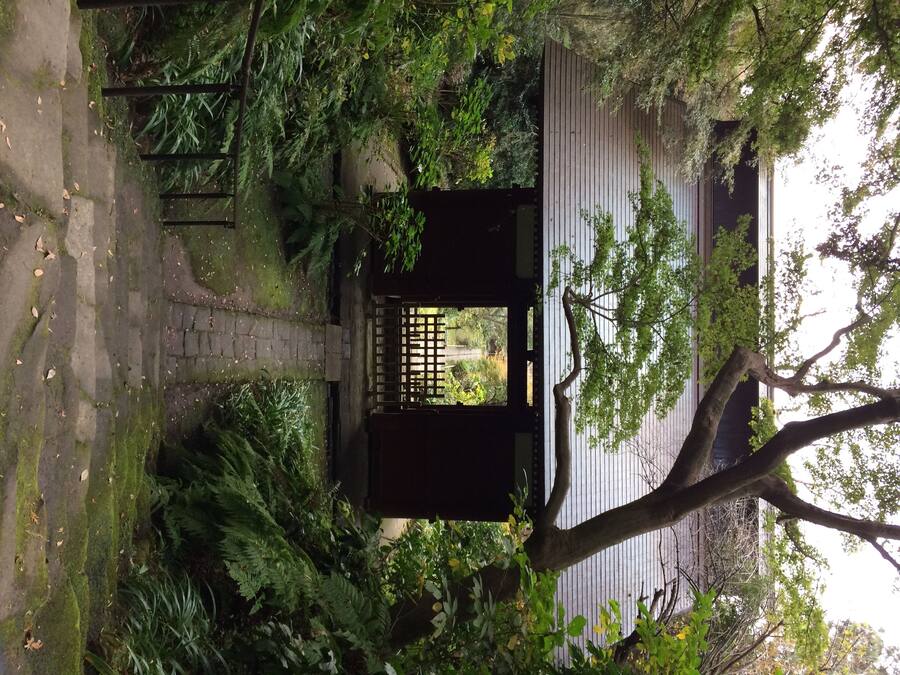 A traditional Japanese gate with a wooden structure and a lattice design, surrounded by lush greenery and a stone pathway.