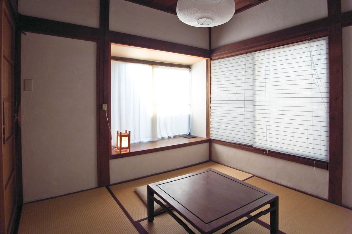 A traditional Japanese room with tatami flooring, a low wooden table, a hanging paper lantern, and shoji screens.