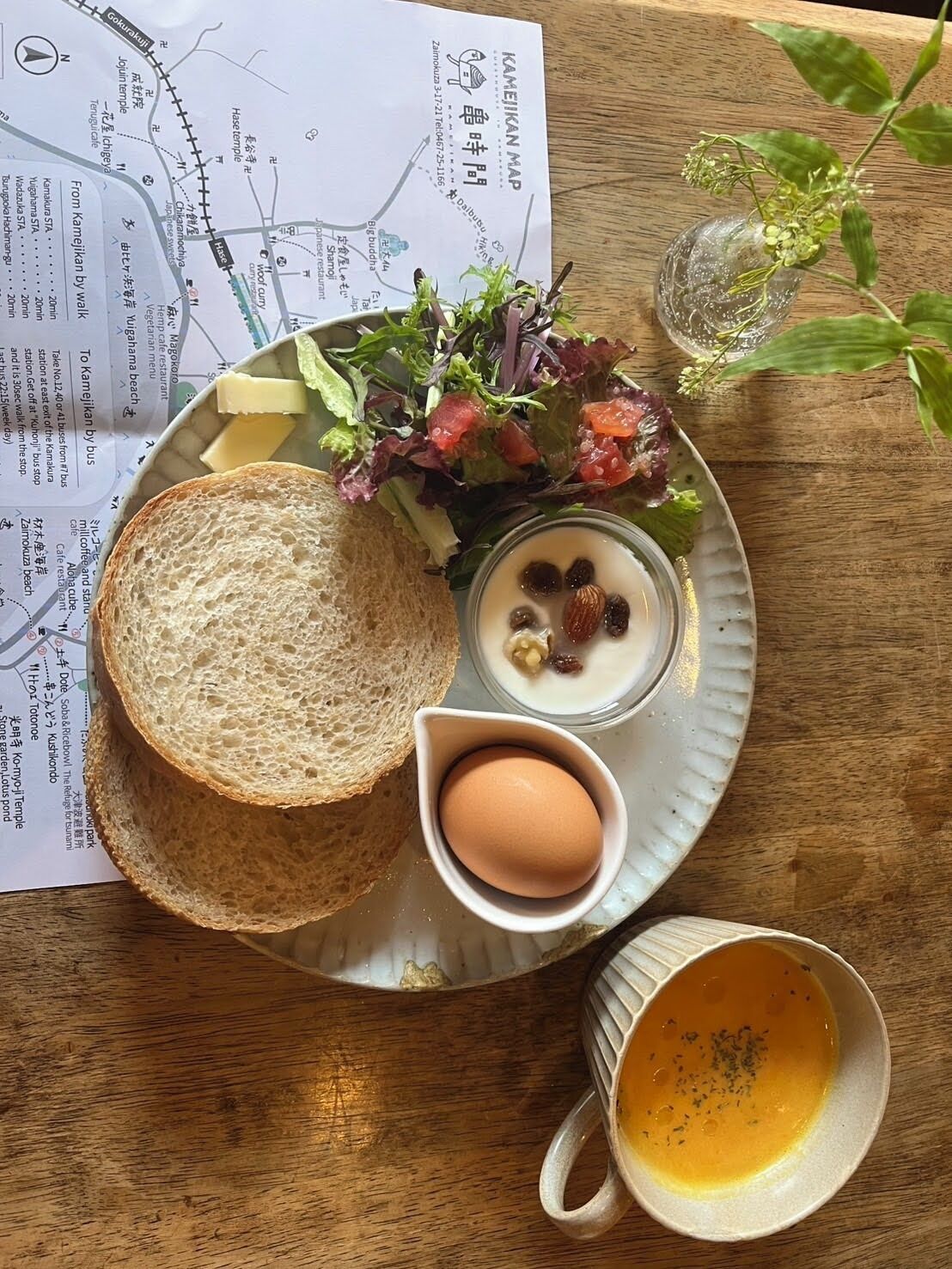 A meal with bread, salad, a bowl of nuts, an egg, and a cup of soup on a wooden table.