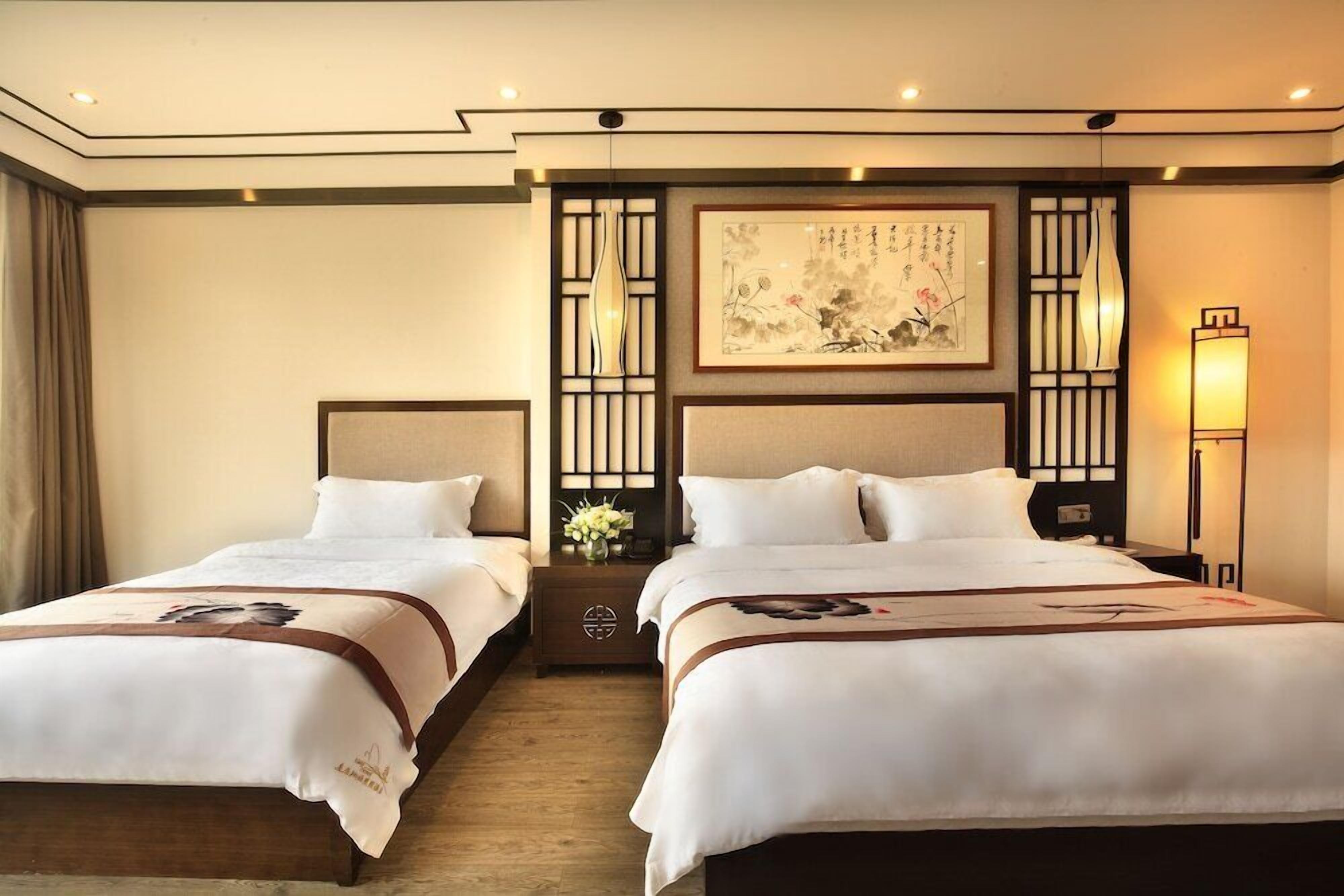 Habitación de hotel con dos camas, una obra de arte grande enmarcada en la pared y una lámpara de estilo tradicional.
