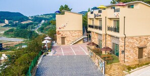 Un hotel con vestíbulo de baldosas de piedra, una escalera que conduce al piso superior y mobiliario exterior con sombrillas.