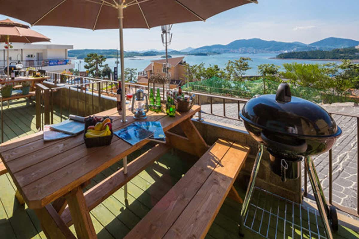 Area pranzo all'aperto con tavolo in legno, barbecue e ombrellone per l'ombra.