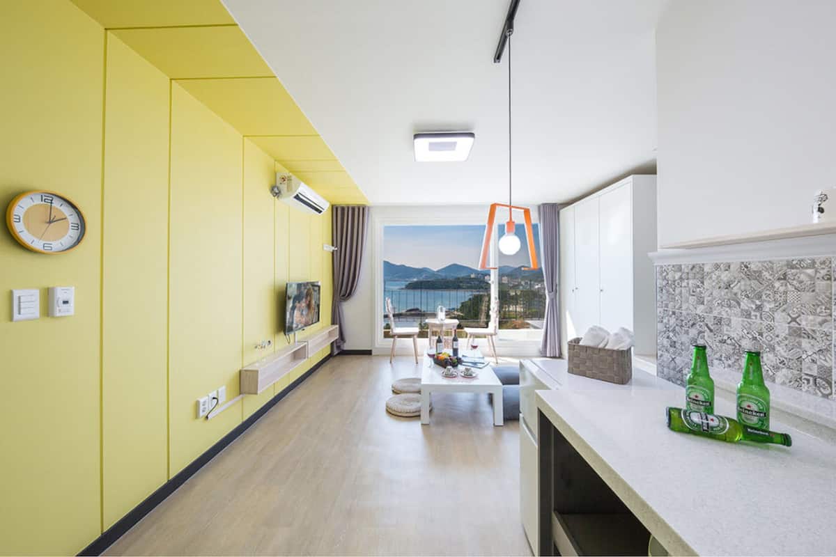 Una stanza luminosa di colore giallo con un'ampia finestra, un soffitto bianco e un tavolo bianco.