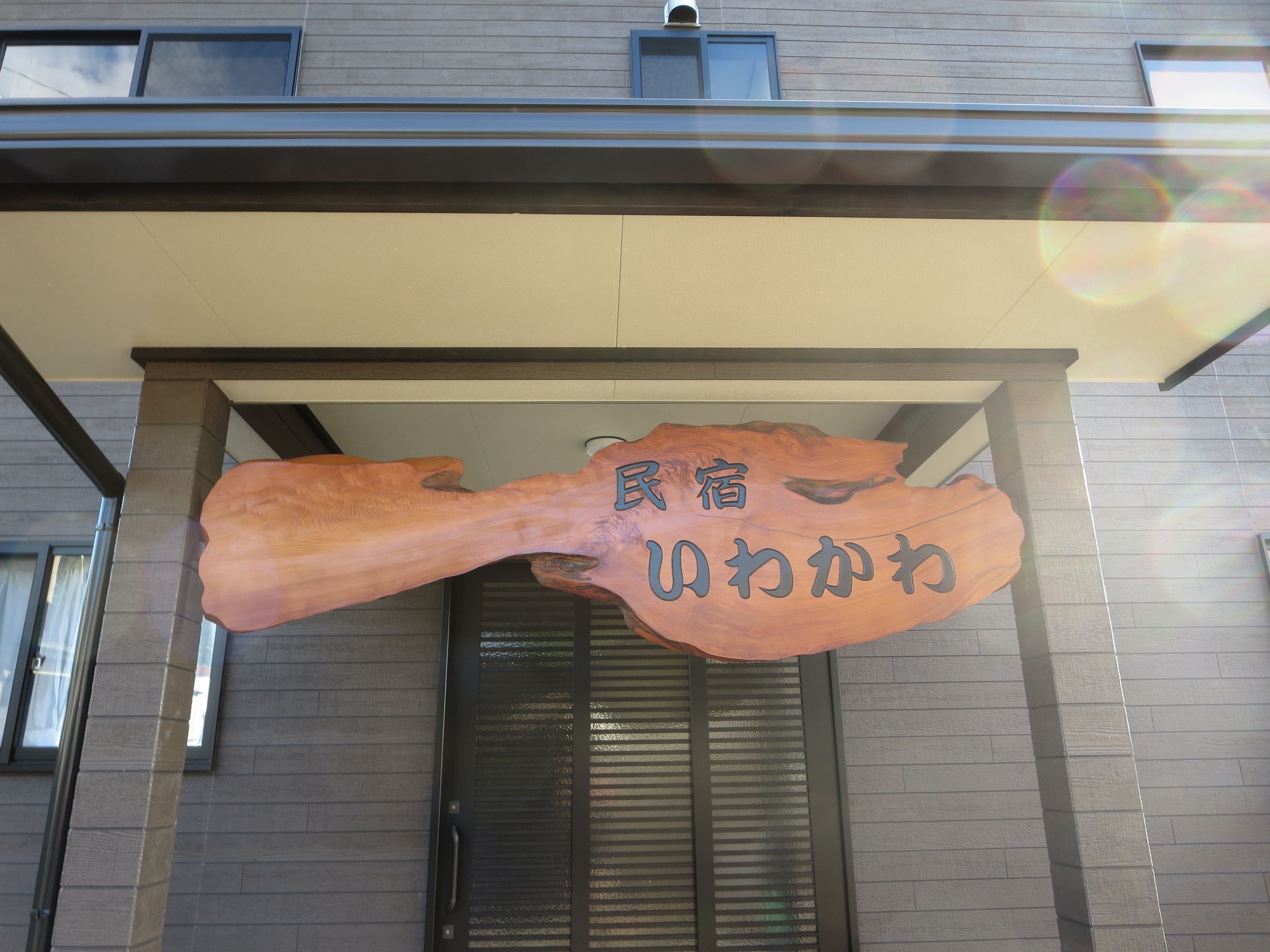 A building entrance with a wooden sign displaying Japanese characters.