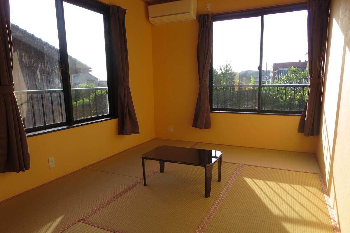 A room with tatami flooring, a small table, and large windows with curtains.