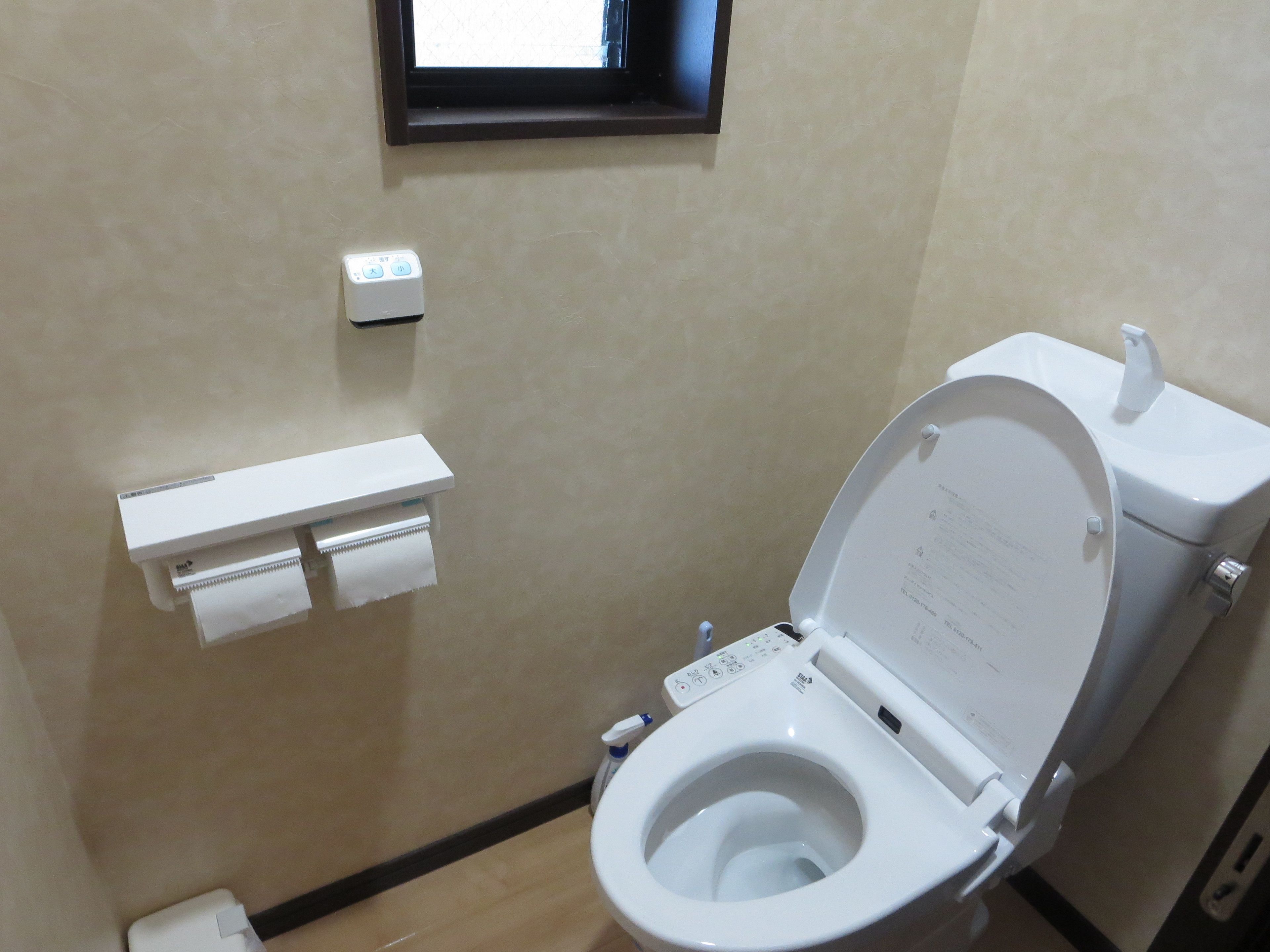 A modern bathroom with a toilet, a hand dryer, and a paper towel dispenser.