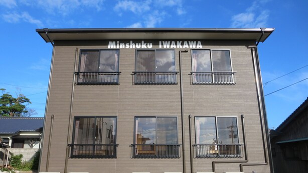 A building with the sign "Minshuku Iwakawa" on the facade, featuring multiple windows and air conditioning units on the ground floor.