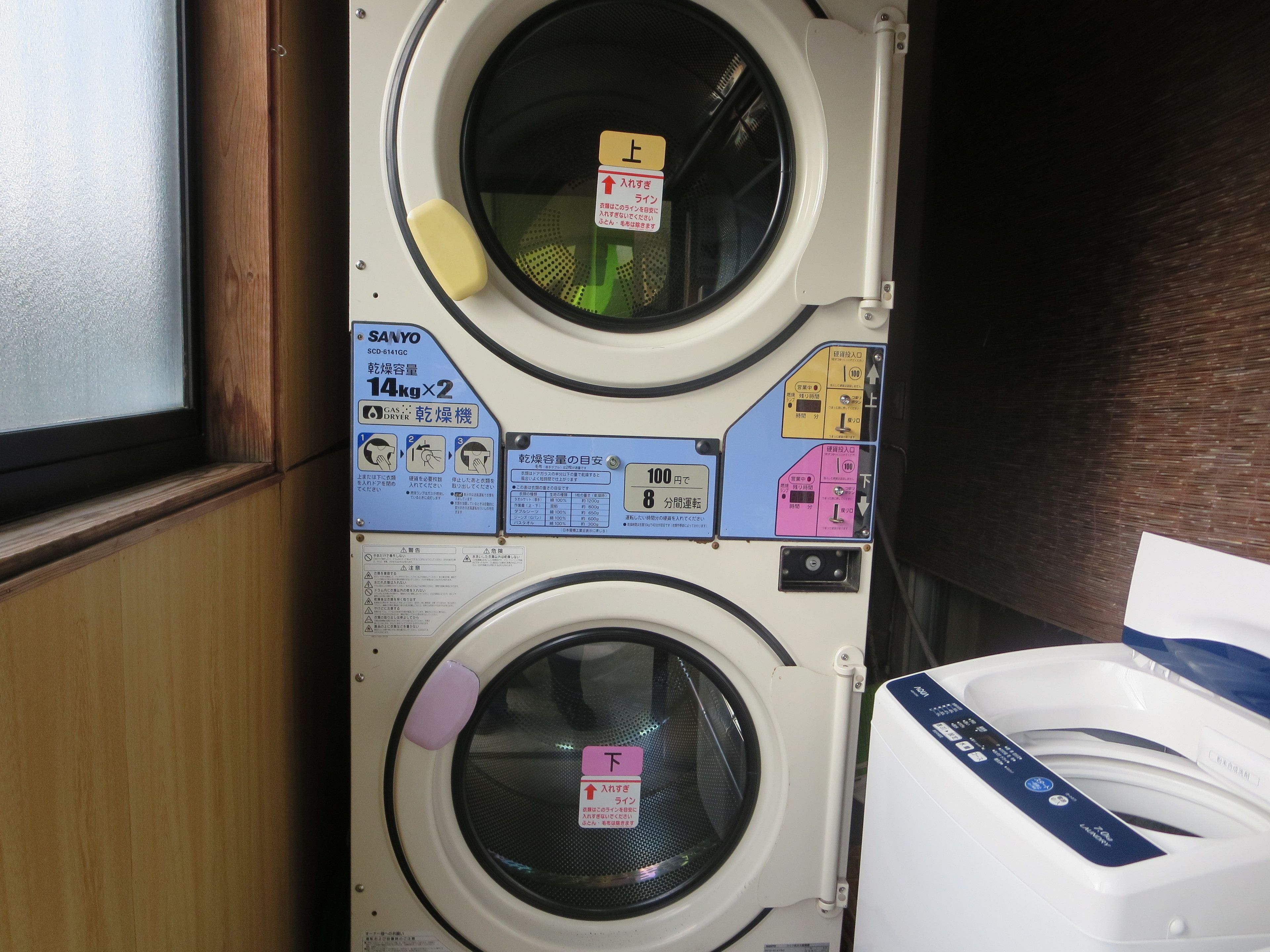 A laundry area with two front-loading washing machines, a dryer, and instructional labels in Japanese.
