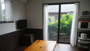 A room with a wooden table, a TV on the wall, a sliding glass door to the outside, and a microwave on a shelf.