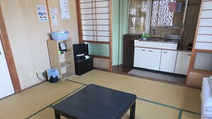 A traditional Japanese room with tatami flooring, a low table, a small TV on a shelf, and a kitchen area with a sink and cabinets.