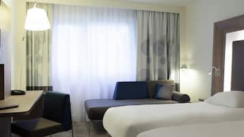 A hotel room with a bed, a desk, a chair, a sofa, and a window with curtains.