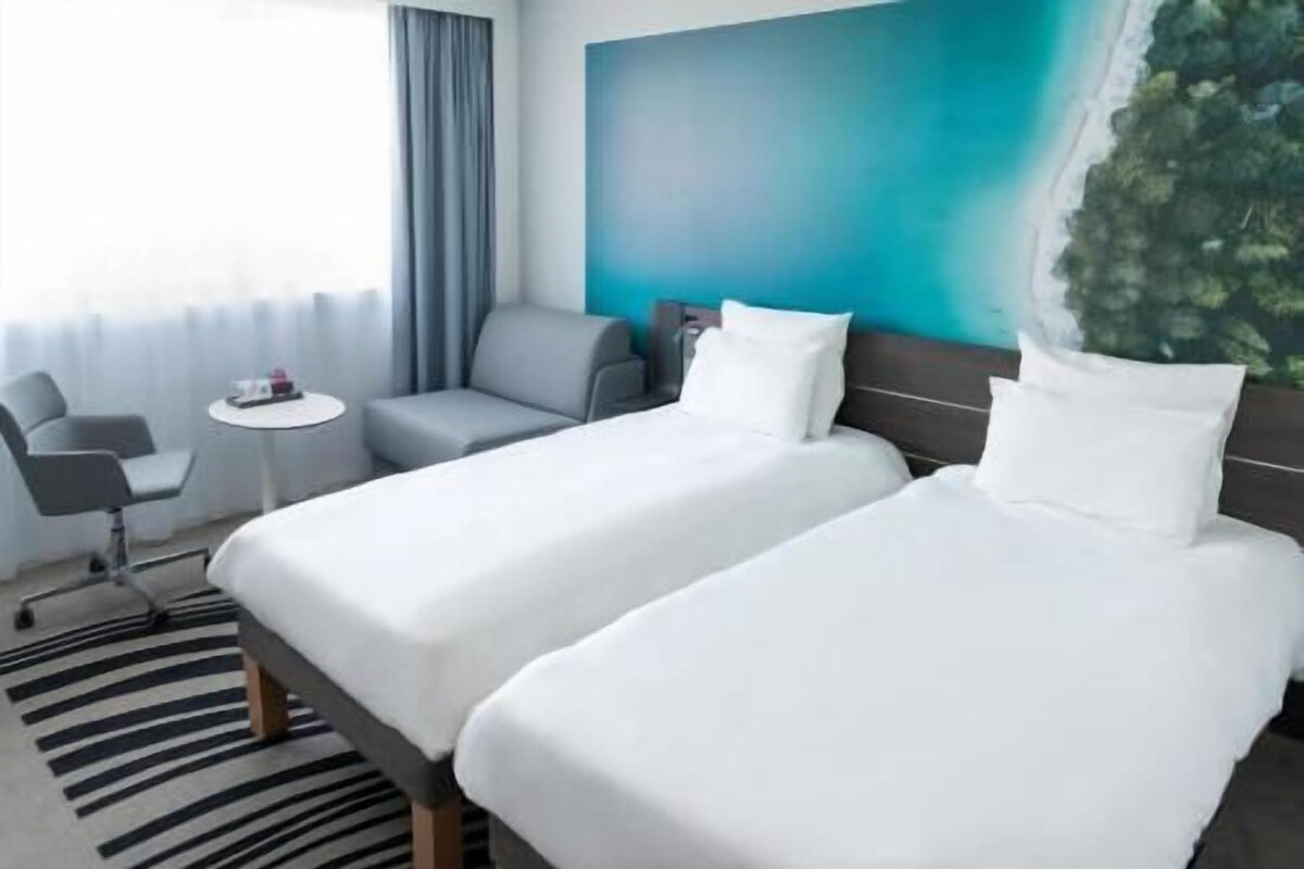 Une chambre d’hôtel avec deux lits, une petite table, une chaise et une vue sur un paysage côtier.