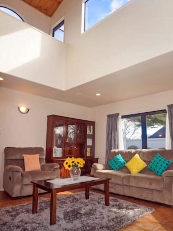 Un salon spacieux avec un plafond haut, un meuble en bois, un canapé agrémenté de coussins colorés et une table basse.