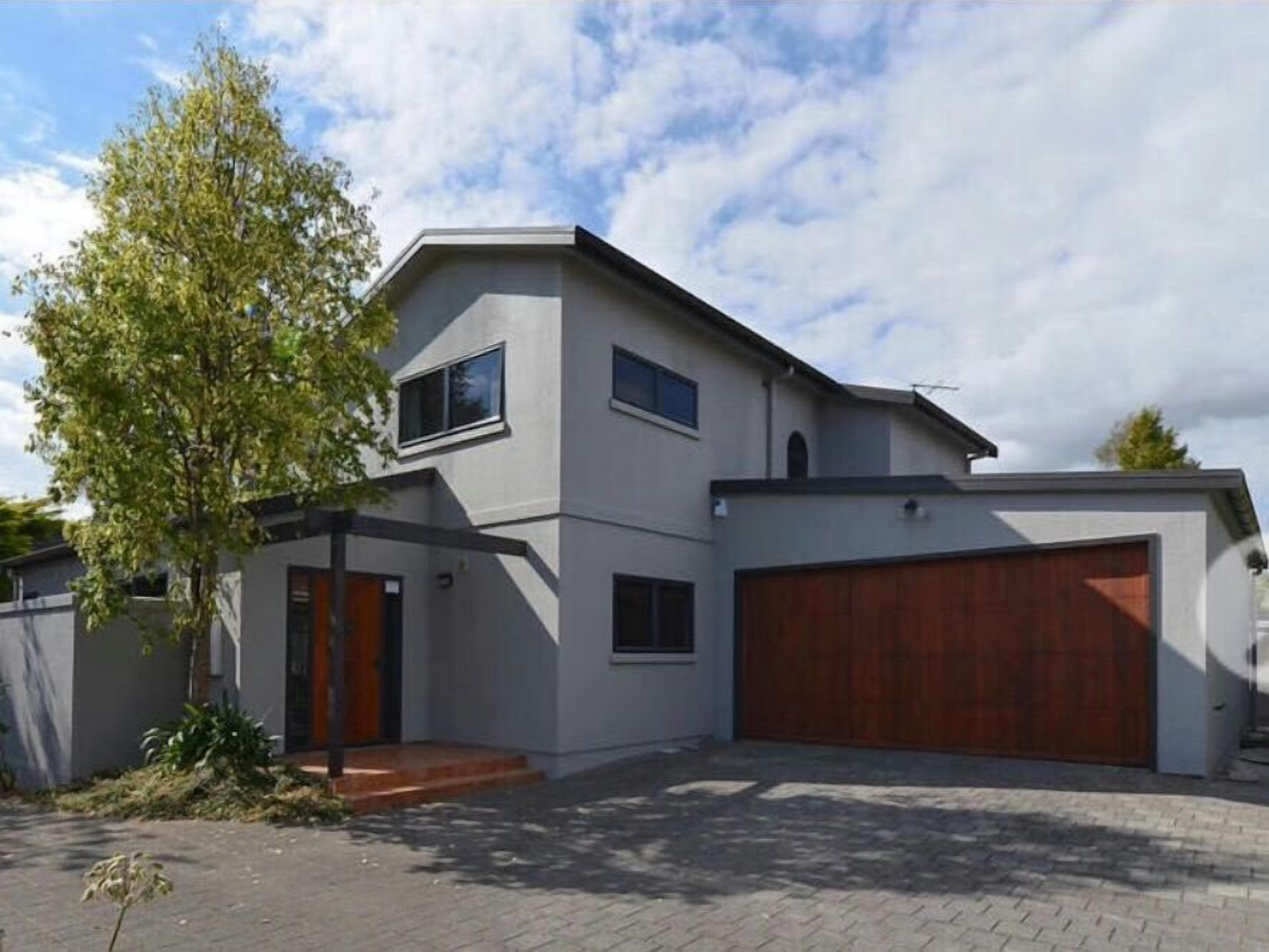 A modern two-story house with a garage, a tree in the front yard, and a clear sky.