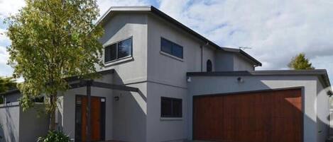 A modern two-story house with a garage, a tree in the front yard, and a clear sky.