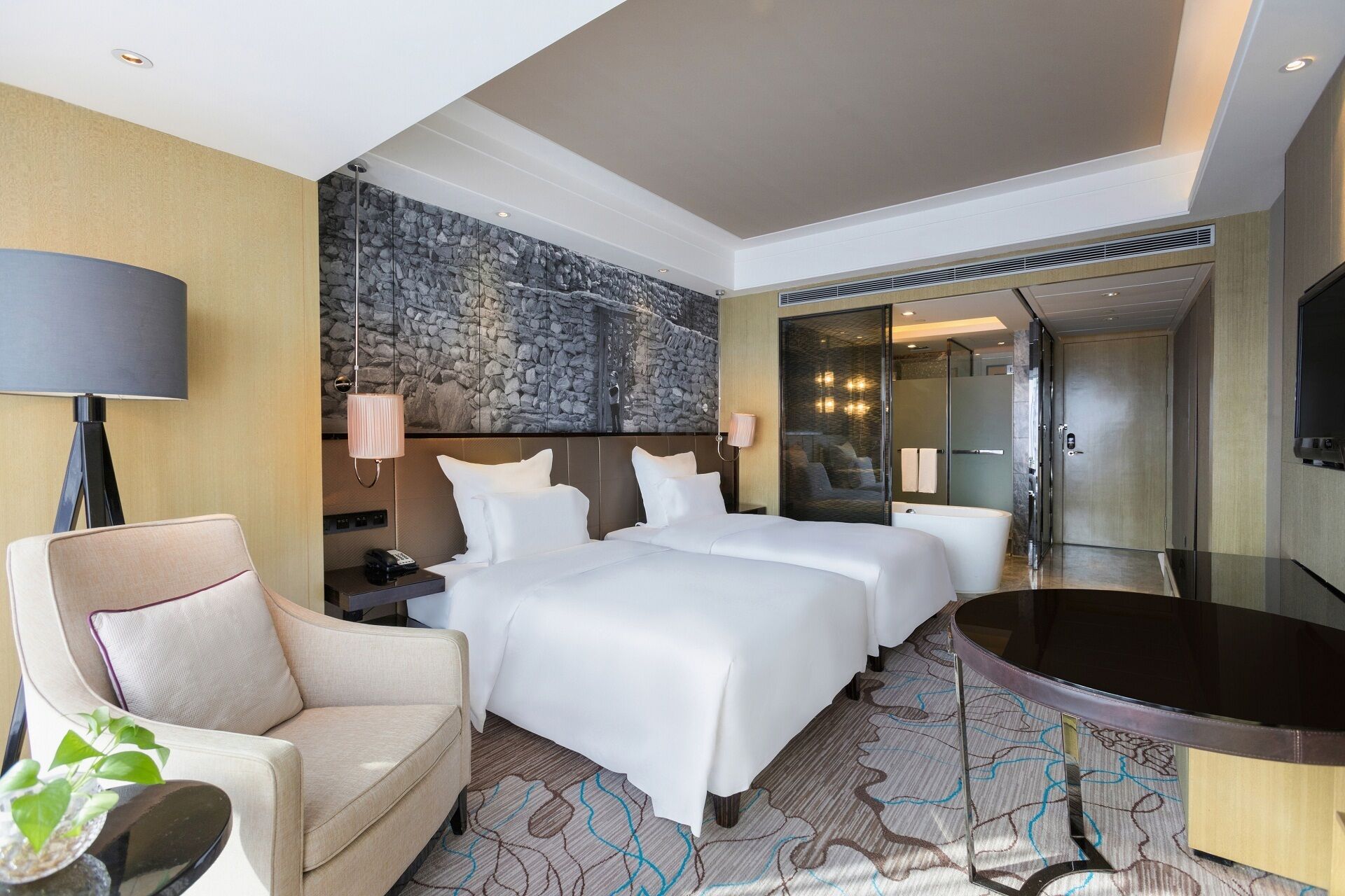 A hotel room with a large bed, a chair, a desk, a mirror, and a bathtub.