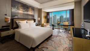 Habitación de hotel con una cama grande, un escritorio, una silla, un televisor y vistas a la ciudad.