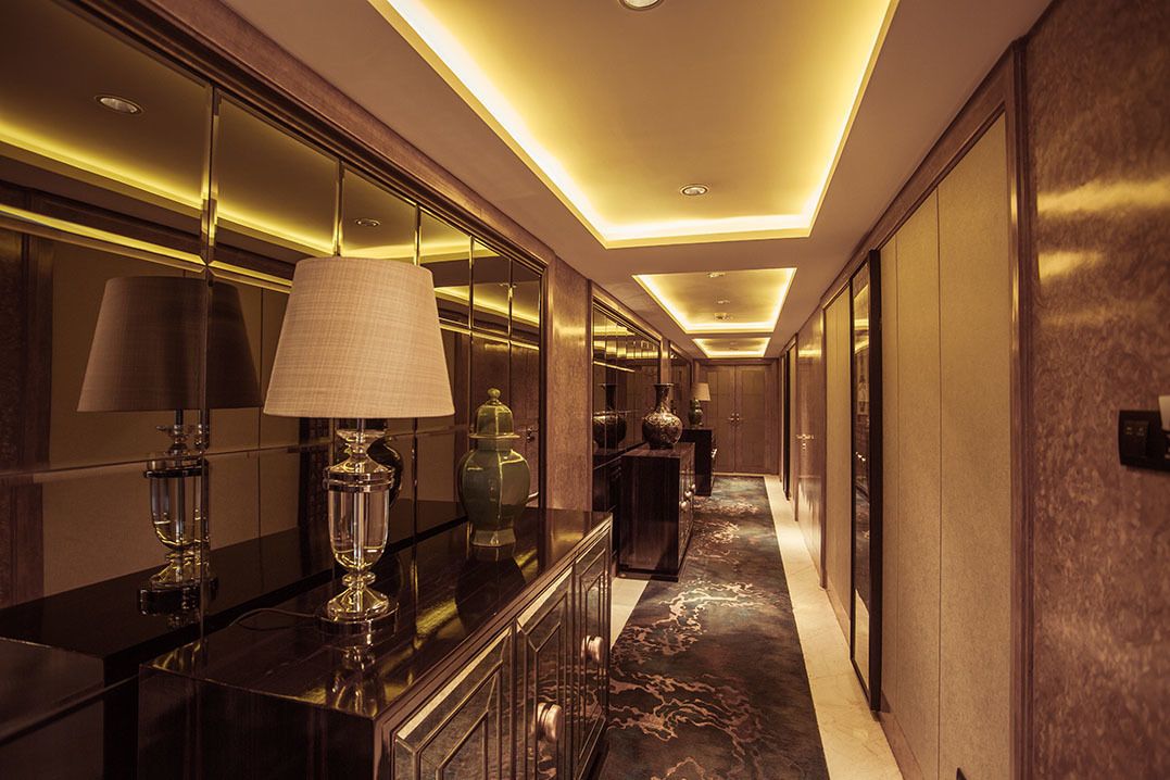 A luxurious hallway with a marble floor, elegant lighting, and a reflective wall.