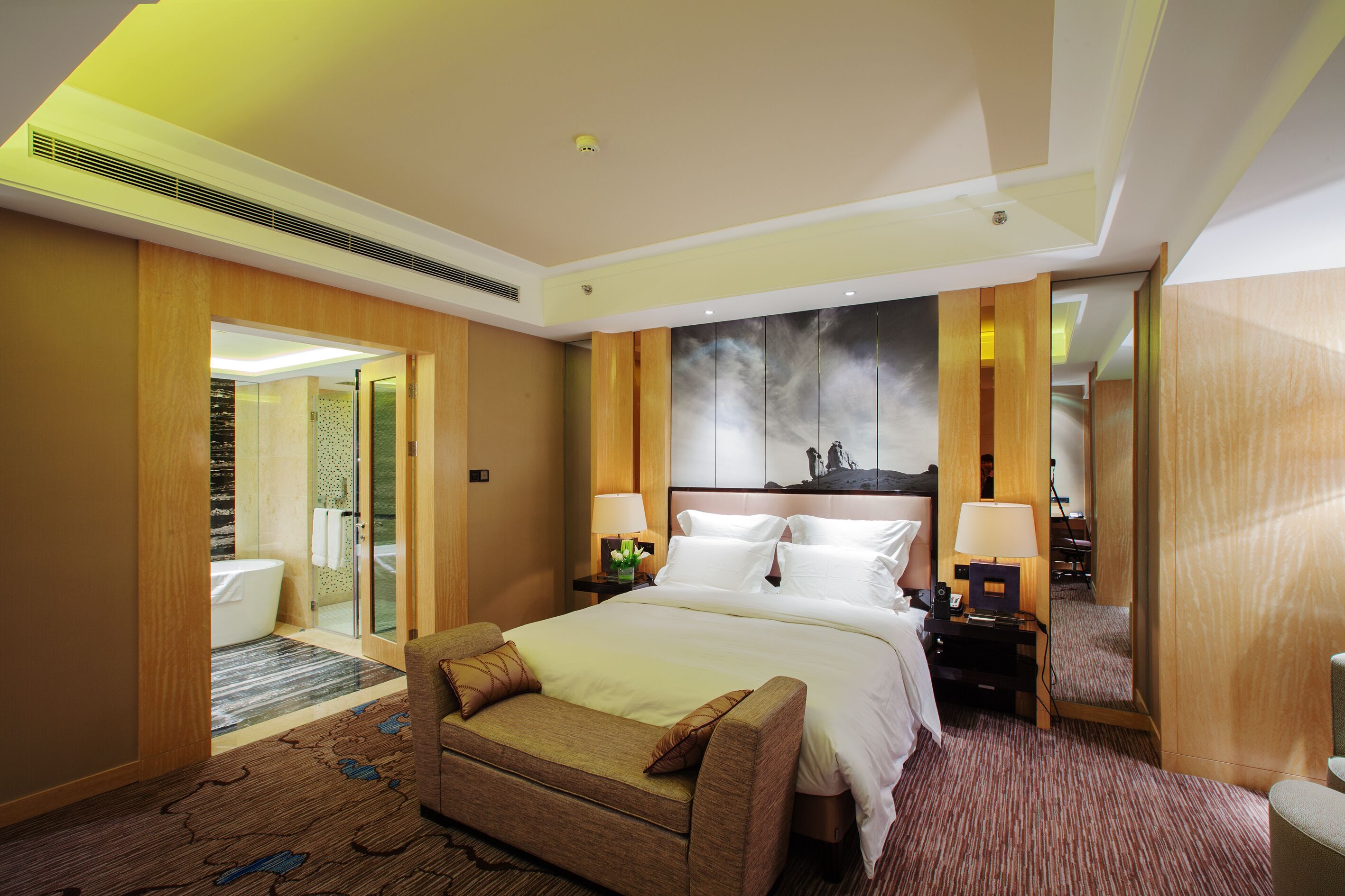 A hotel room with a large bed, a sitting area, a bathroom with a bathtub, and a large mirror.