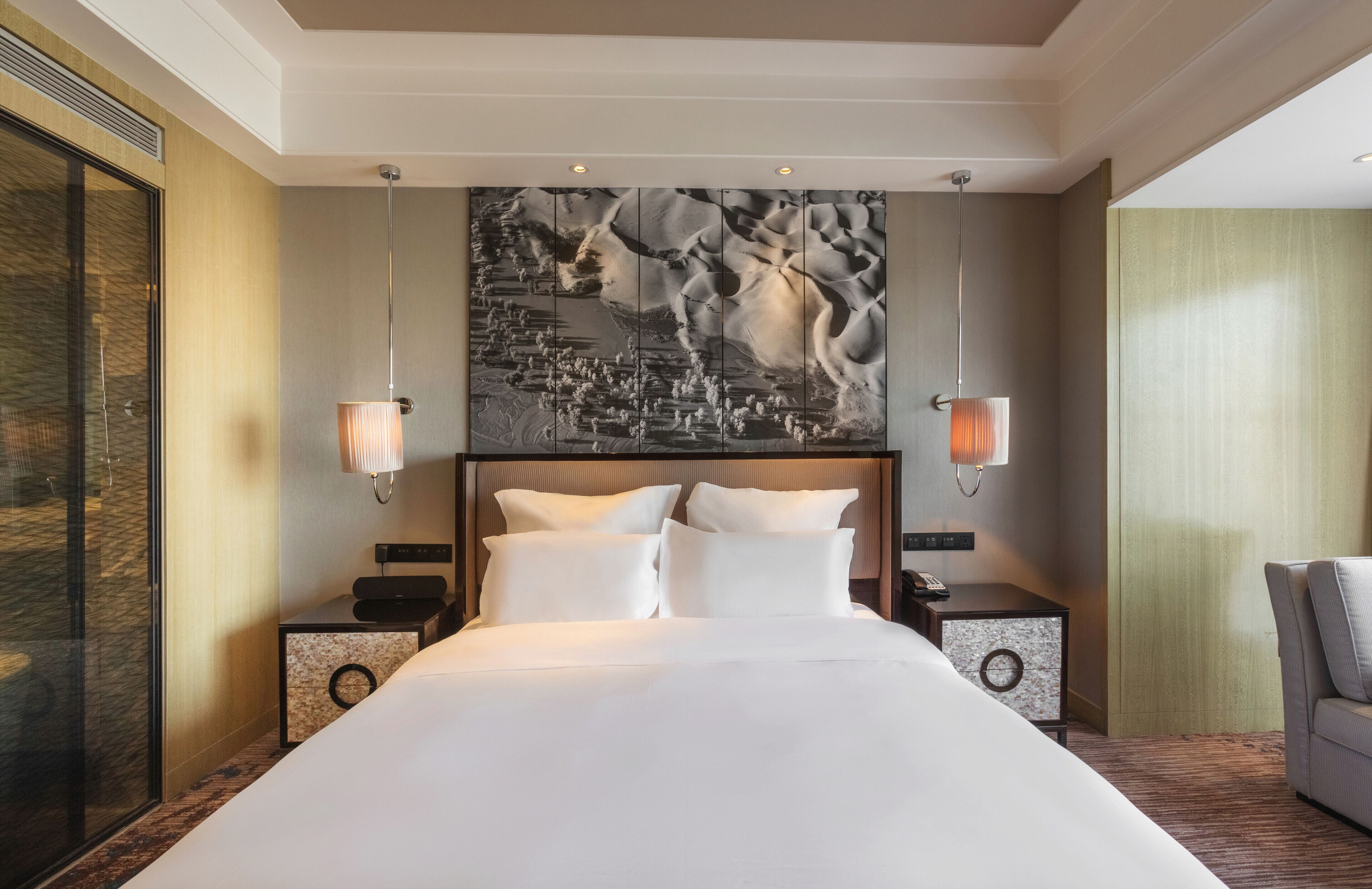 Habitación de hotel con una cama grande, dos mesitas de noche, una obra de arte en la pared y un separador de vidrio.