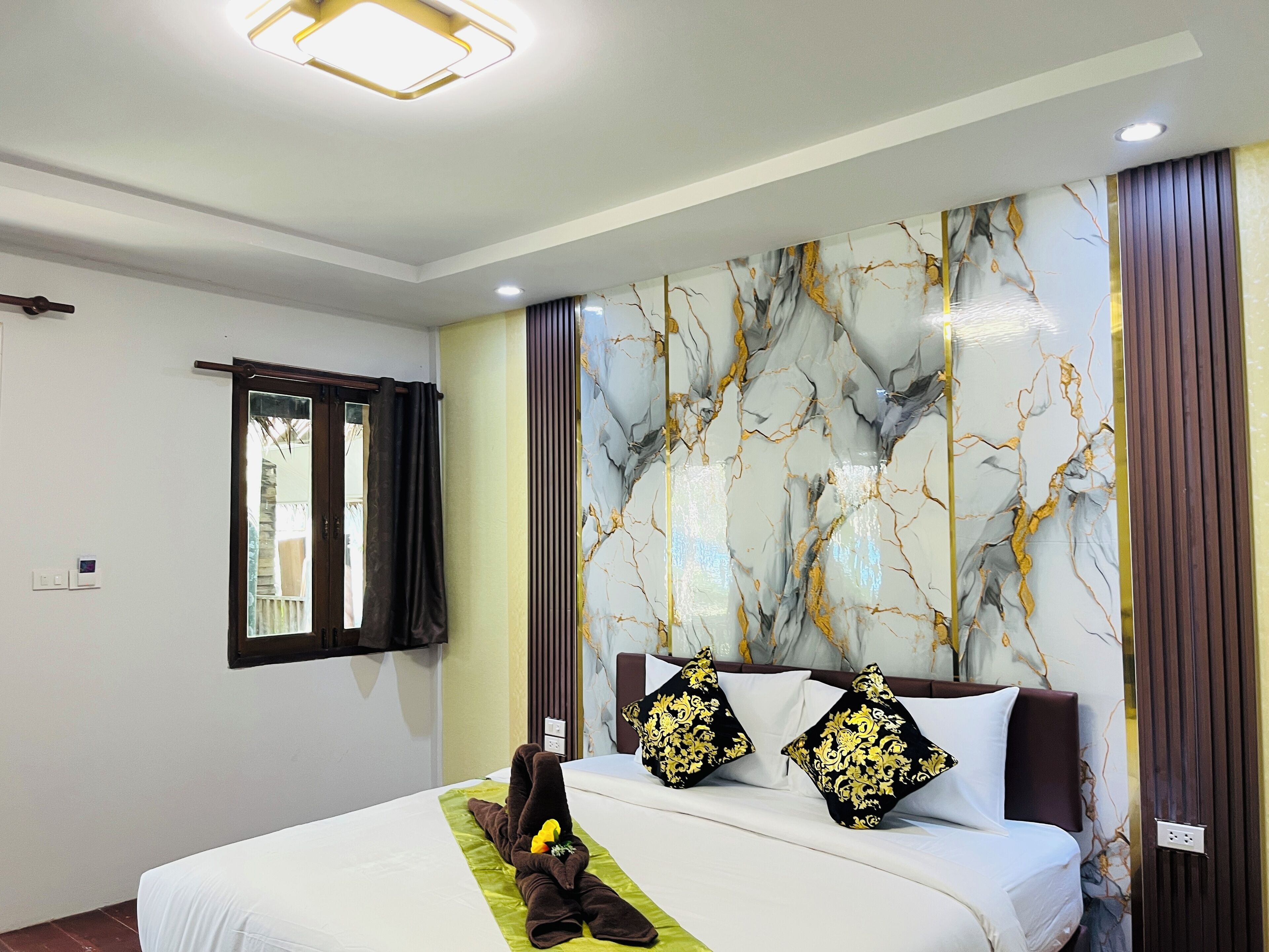 A hotel room with a bed, a window with curtains, a wall with a marble-like pattern, and a ceiling light fixture.