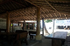 An outdoor covered seating area with wooden tables and benches, a thatched roof, and a sign in the background. - New Ozone Resort & Spa (Ko Lanta)