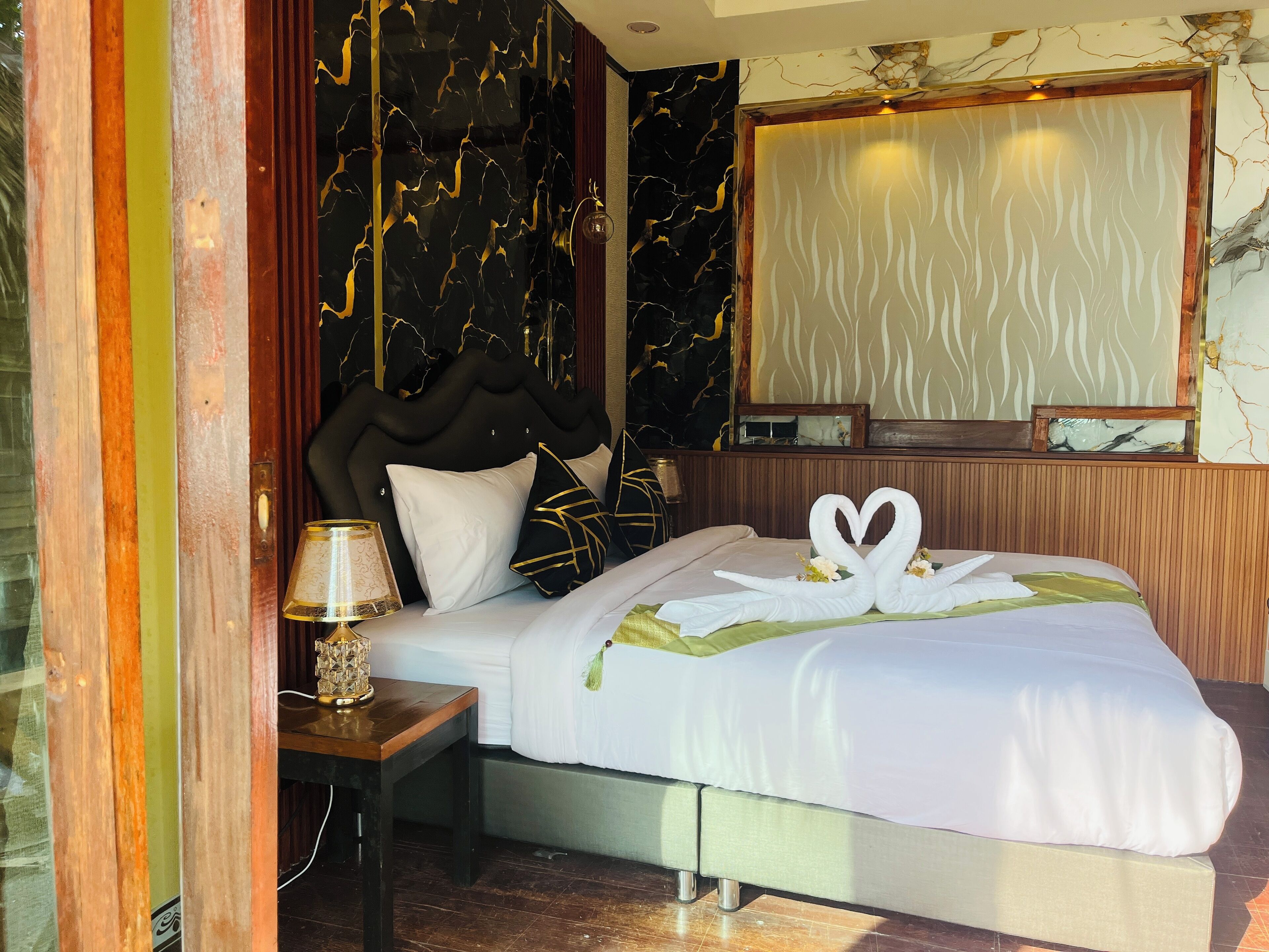 A hotel room with a bed, a nightstand, a lamp, a mirror, and a wall with a marble-like pattern.