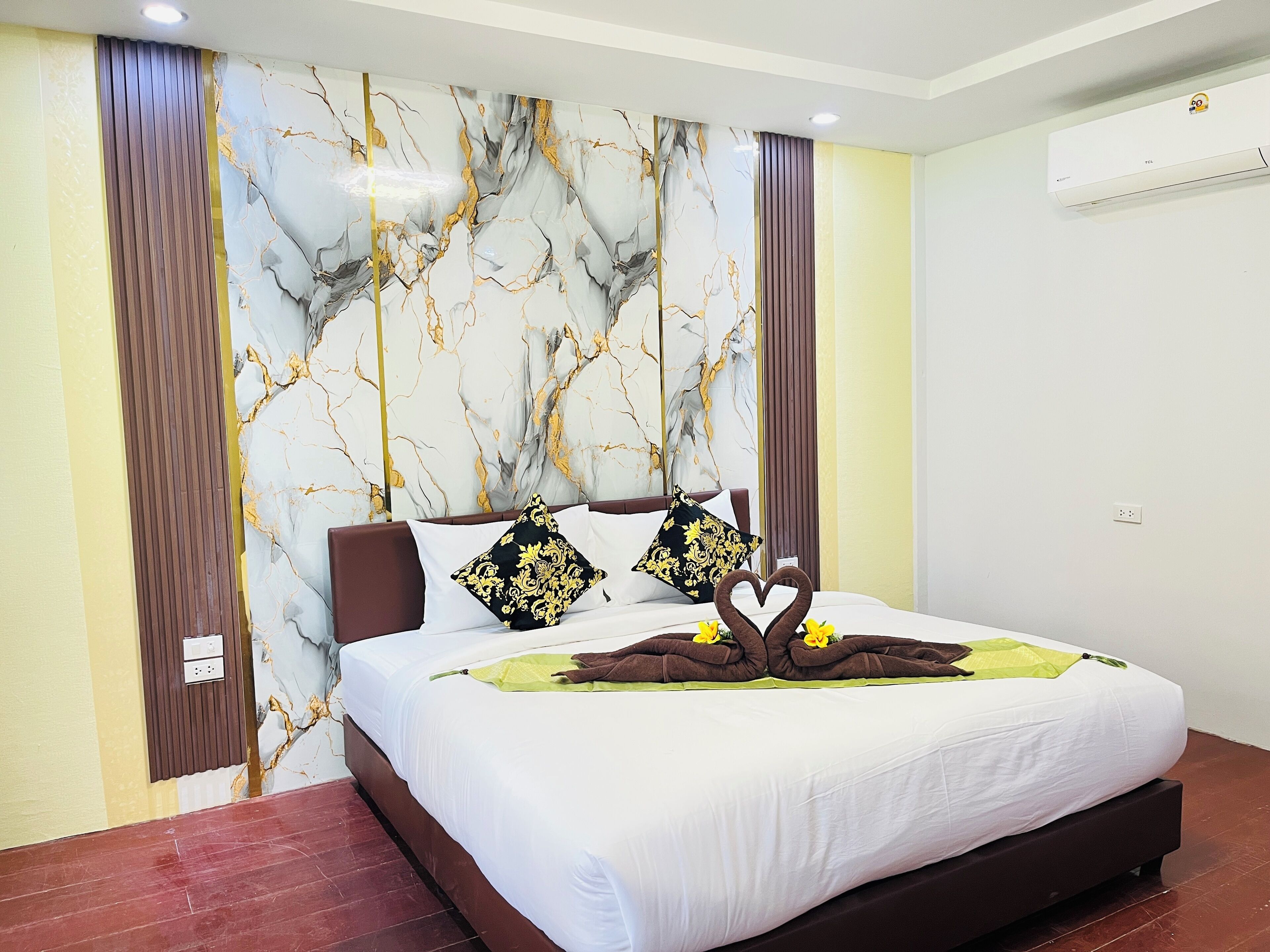 A hotel room with a marble-patterned headboard, a neatly made bed with a heart-shaped towel arrangement, and a modern air conditioning unit on the wall.