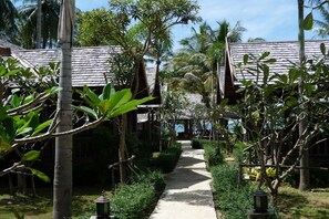A pathway leading to a traditional wooden building with a thatched roof, surrounded by lush greenery and palm trees. - New Ozone Resort & Spa (Ko Lanta)
