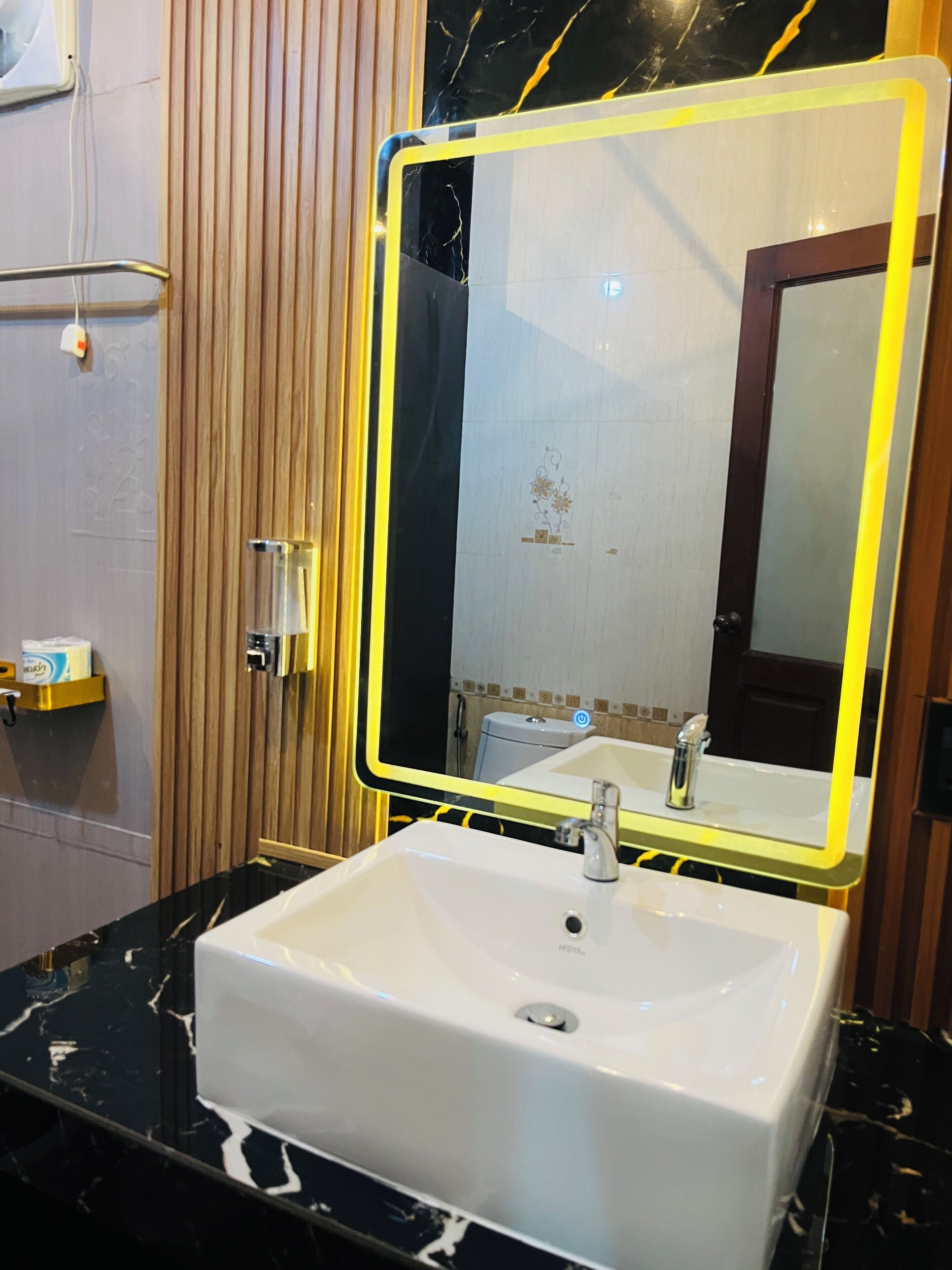 A bathroom with a white sink, a mirror with a yellow frame, and wooden paneling on the wall.