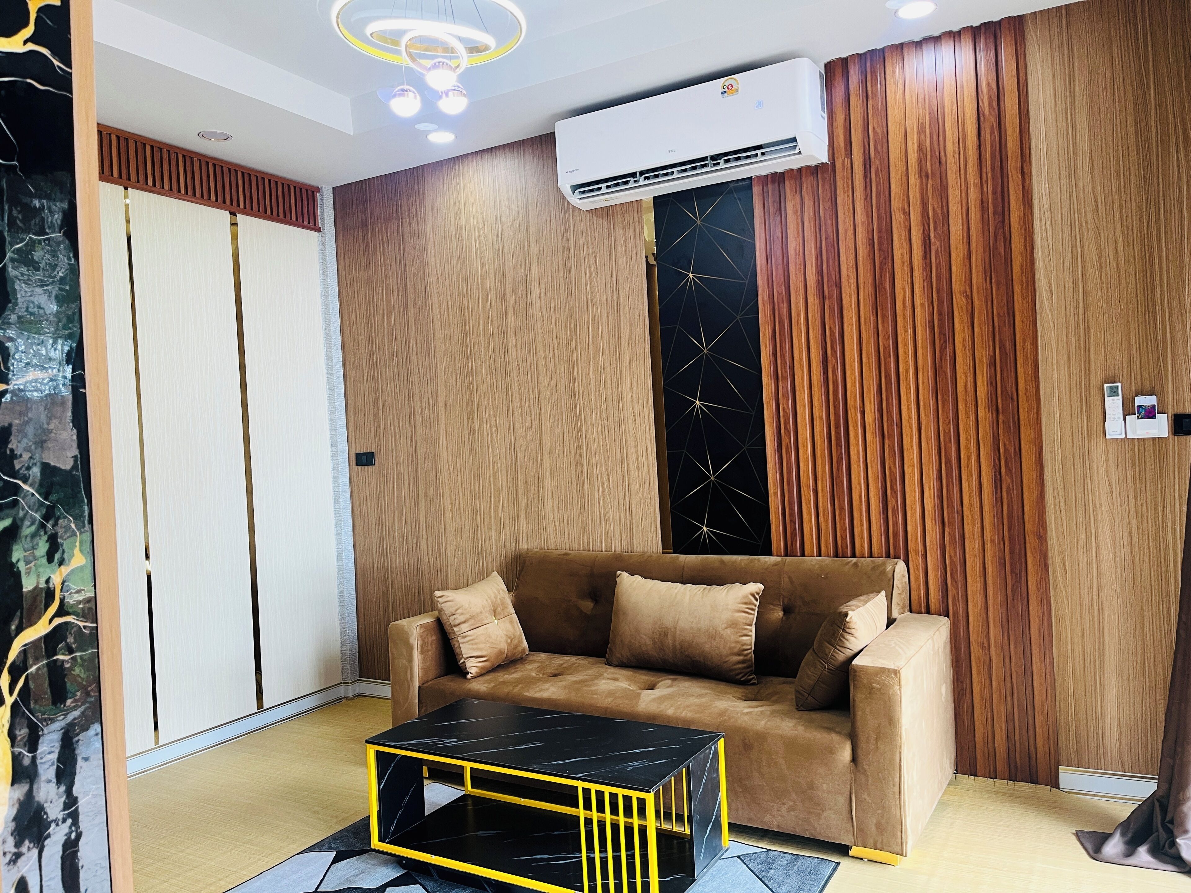 A modern living room with a brown sofa, a black coffee table, and wooden paneling on the walls.