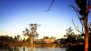 A serene lakeside scene with a clear sky, a few trees, and a building in the background. - The Woolshed at Jondaryan - Campsite (Jondaryan)
